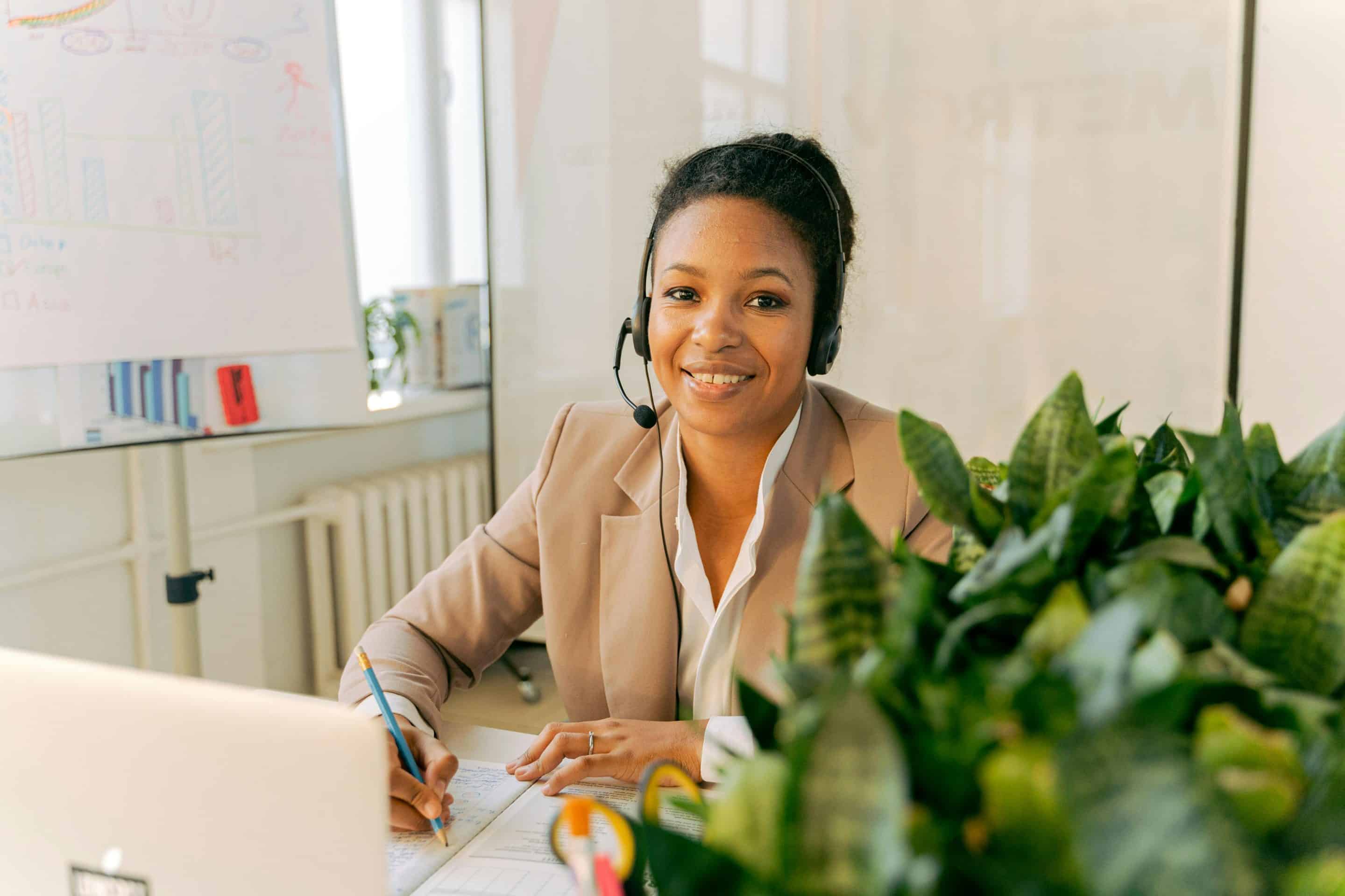courtier en crédits Conseillère en crédit immobilier avec headset travaillant avec son ordinateur protable, crayon à la main, dans son bureau